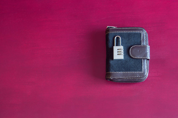 Un cadenas à mot de passe numéroté argent fermé sur un portefeuille zippé en cuir bleu vintage sur un fond studio texturé coloré avec espace de copie. Concept de sécurité et de finance. - Photo, image