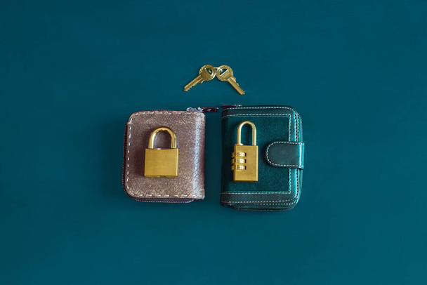 Two elegant and classic vintage wallets with a golden padlock on top of each one on a colorful textured background and two keys together. Finances and couple economics. - Photo, Image