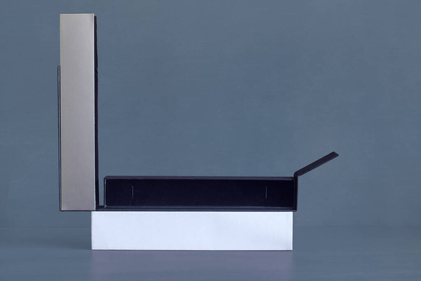 Una larga y delgada caja rectangular con la tapa gris plateada abierta, revelando el aterciopelado azul del interior vacío. Regalos y embalajes. - Foto, imagen