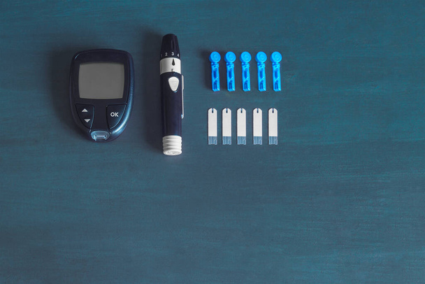 Ένα γλυκόμετρο και τις προμήθειες του για τον έλεγχο των επιπέδων σακχάρου στο αίμα. Μπλε έννοια διαβήτη υποβάθρου. - Φωτογραφία, εικόνα