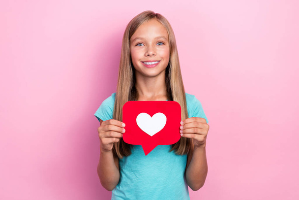 Photo of good mood pretty little child dressed teal t-shirt holding heart like postcard isolated pink color background. - Foto, Imagen