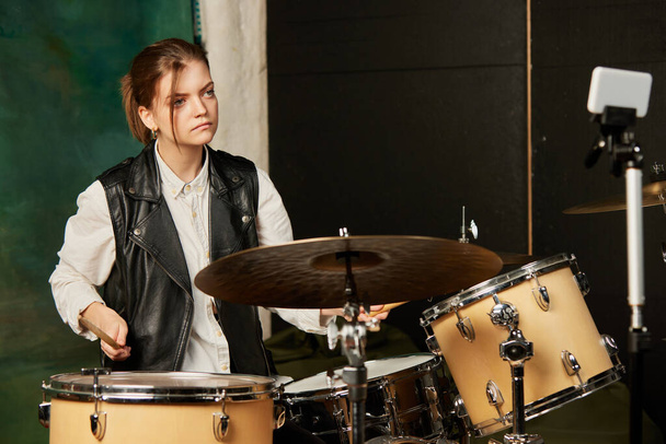 Emotional young girl, rock musician recording music video blog home lesson, playing drums or making broadcast internet tutorial while sitting at record label. Concept of hobby, music, art. - Foto, Imagem