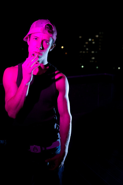 Handsome young man lit with colorful lights standing on a roof a - Fotografie, Obrázek