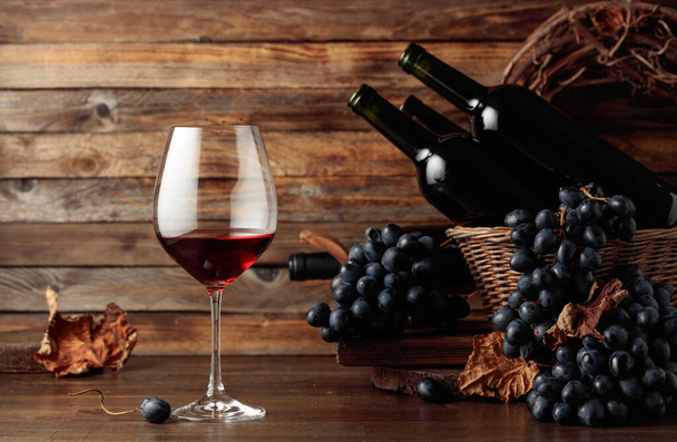 Red wine and blue grapes. Wine and grapes in a vintage setting on an old wooden table. - Photo, Image