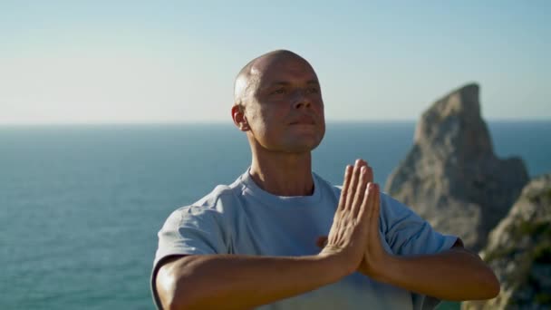 Yoga yapan bir sporcu okyanus manzarası. Odaklanmış bir adam güzel bir uçurumun kenarında namaste pozisyonunda meditasyon yapıyor. Kel yakışıklı adam güneş ışığında dışarıda dinleniyor. Farkındalık konsantrasyon konsepti. - Video, Çekim