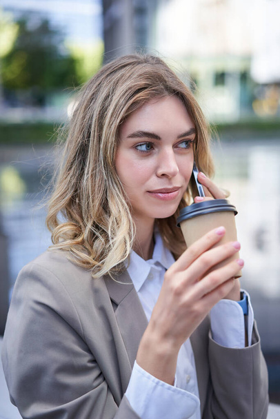 Porträt einer schönen Frau, die mit dem Handy telefoniert und Kaffee trinkt. Geschäftsfrau trinkt Imbiss in der Innenstadt und ruft jemanden an. - Foto, Bild