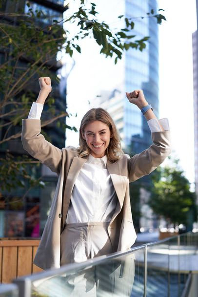 Saleswoman expresses joy and happiness. Businesswoman triumphing on street, raising hands up, celebrating victory, smiling pleased. - Foto, imagen