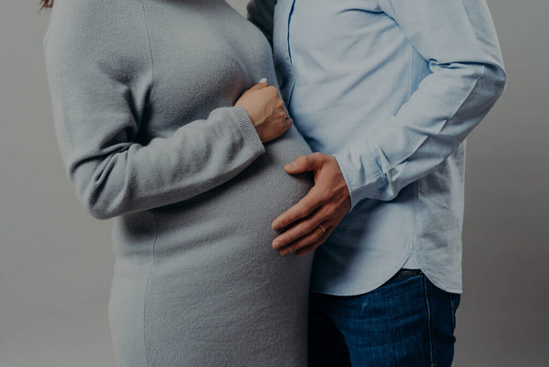 Pregnant wife wears dress poses near husband who touches her big belly. Future mothr and father wait for new member of family. Parenthood concept - Photo, Image