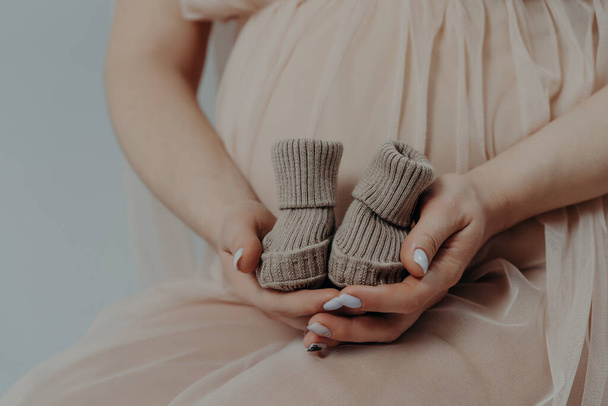 Conceito de maternidade e gravidez. A mãe expectante prepara-se para dar à luz à criança mantém botas em poses de mãos interiores que estão no terceiro trimestre - Foto, Imagem