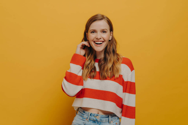 Be Happy. Positive laughing millennial woman in casual clothes smiling after hearing funny joke or ridiculous anecdote from friend, posing isolated over yellow studio background. Positiveness concept - Photo, Image