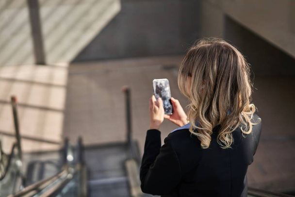Portrét korporátní ženy stojící na eskalátoru, telefonování, používání smartphonu, procházky ve městě. - Fotografie, Obrázek