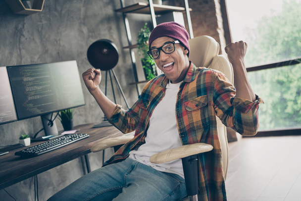 Photo of cheerful successful freelancer wear hat glasses celebrating great job offer indoors workplace workstation loft. - Foto, imagen