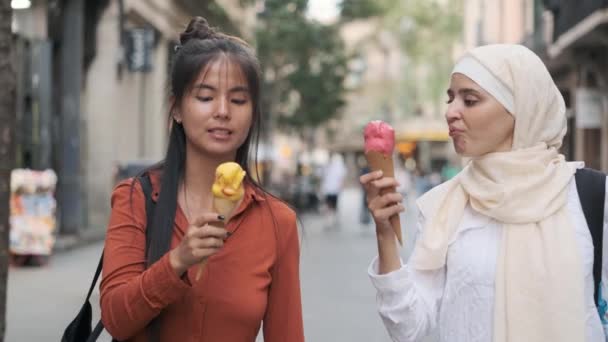 Amici femminili multietnici che si divertono a mangiare coni gelato mentre camminano all'aperto per strada. Amicizia concetto. - Filmati, video