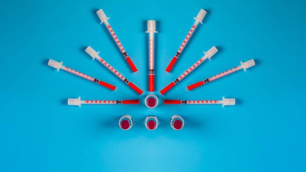 Insulin injection syringe arrayed around a insulin injection solution in ,in shape of a sun on blue background.Top view. - Fotografie, Obrázek