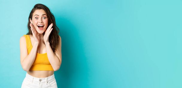 Summer and lifestyle concept. Young cheerful woman look with surprised face at camera, react to awesome good news, smiling and cheering, standing against blue background. - Fotoğraf, Görsel