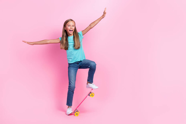 Full length photo of excited funky little child dressed teal t-shirt riding skateboard empty space isolated pink color background. - Φωτογραφία, εικόνα