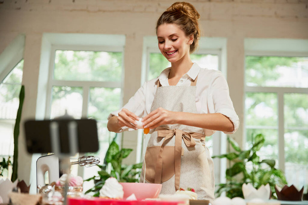 Young beautiful girl culinary specialist writes video blog on baking. Smiling female vlogger or shooting blog filming reportage advertising video. Hobbies and leisure activities. - Fotoğraf, Görsel
