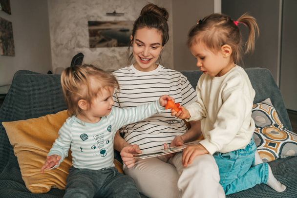 Joyous female parent with the book seated on the sofa watching her kids playing with a toy - Фото, зображення