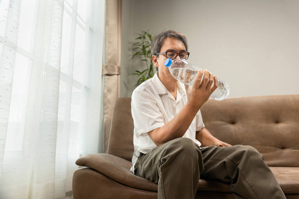 Starszy Azjata trenuje butelkę wody w domu, aby zachować swoją masę mięśniową, zapobiec sarkopenii i resorpcji kości. - Zdjęcie, obraz