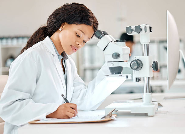Ik ga haar bevindingen voor. een jonge wetenschapper die notities schrijft terwijl hij een microscoop gebruikt in een lab - Foto, afbeelding