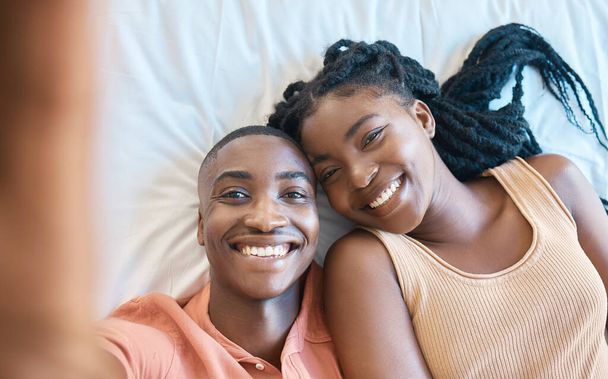 Mutlu Afro-Amerikan çifti yan yana yatarken selfie çekiyorlar. Genç, kaygısız çift yatak odalarında dinleniyor ve birlikte vakit geçiriyorlar.. - Fotoğraf, Görsel