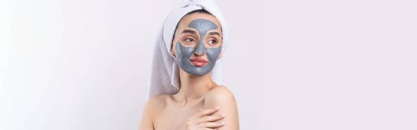 A woman with a gray clay cosmetic mask in a white towel on her head on a white background. - Foto, Imagem
