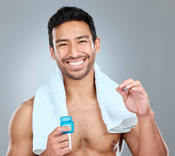 Η ανθοφορία είναι μια σημαντική συνήθεια στοματικής υγιεινής. ένας άντρας που χρησιμοποιεί οδοντικό νήμα ενώ στέκεται πάνω σε γκρι φόντο - Φωτογραφία, εικόνα