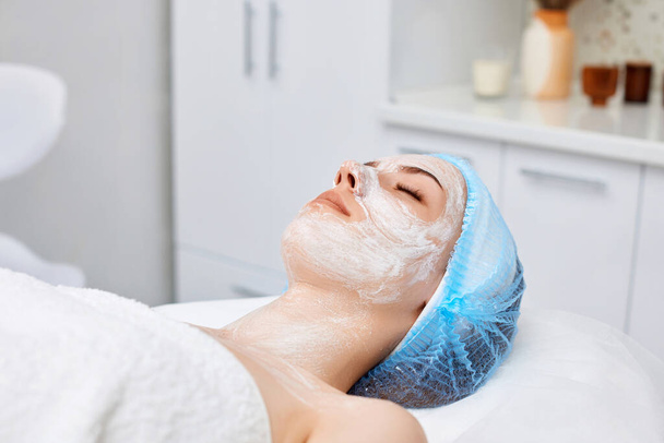 beautiful woman with white moisturizing mask on face in the spa salon. close-up - Photo, Image