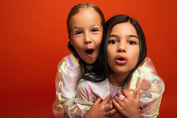 funny preteen girls looking at camera and grimacing with open mouths isolated on orange - Фото, изображение