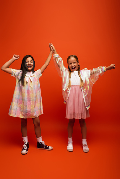 full length of excited girls giving high five and showing win gesture on orange background - Фото, зображення