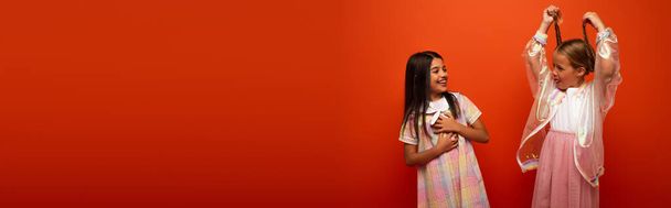 lustiges Mädchen mit Zöpfen und herausgestreckter Zunge neben lachendem Freund isoliert auf orangefarbenem Banner - Foto, Bild