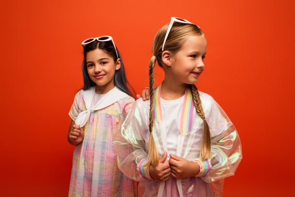 smiling girl in dress touching shoulder of friend with pigtails isolated on orange - Photo, image