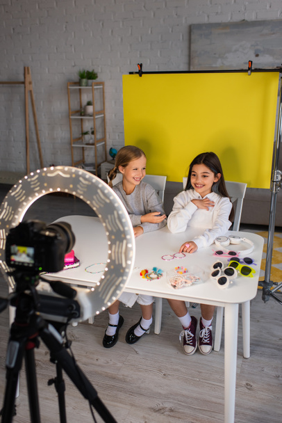 smiling preteen video bloggers talking near different accessories and digital camera in ring light on yellow background at home - 写真・画像