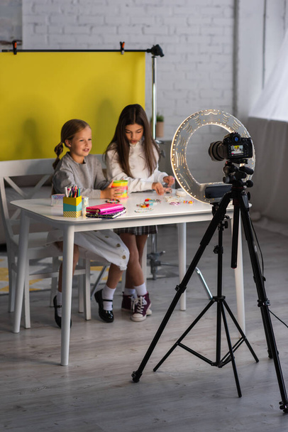 круглая лампа и цифровая камера на штативе рядом с девочками-подростками запись видео блог на желтом фоне дома - Фото, изображение