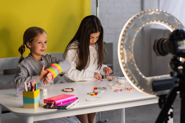 подростковые блогеры со спиральной игрушкой и браслетами с бисером рядом с цифровой камерой с кольцевым светом на размытом переднем плане - Фото, изображение
