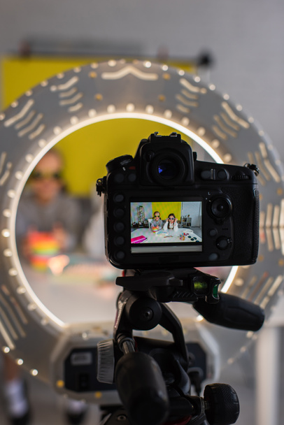 selectieve focus van videocamera in cirkellamp met milde bloggers in trendy zonnebril op scherm - Foto, afbeelding