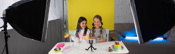 meninas alegres mostrando brinquedo em espiral durante a gravação de vídeo blog no fundo amarelo em casa, banner - Foto, Imagem
