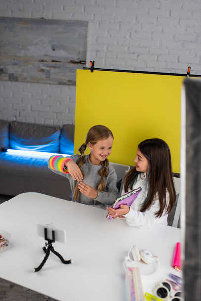 usměvaví bloggeři s notebookem a spirálovou hračkou mluví před smartphonem na držáku - Fotografie, Obrázek