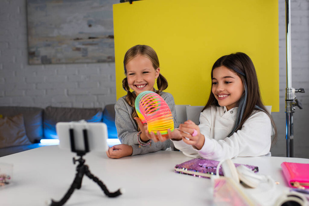 cheerful video bloggers showing spiral toy on yellow background in front of mobile phone at home - Fotoğraf, Görsel