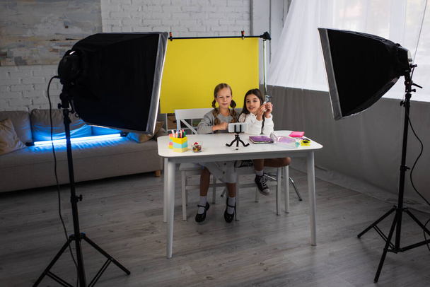 Preteen Mädchen sprechen während Videoblog auf gelbem Hintergrund in der Nähe von Lampen zu Hause - Foto, Bild