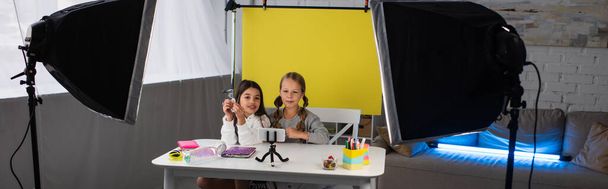 preteen friends recording video blog on cellphone on yellow background near lamps at home, banner - Photo, Image