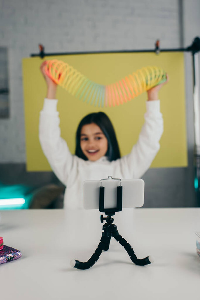 blurred video blogger holding spiral toy in raised hands near mobile phone on holder - 写真・画像