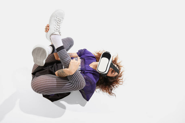 Ritratto di ragazza sdraiata sul pavimento in strana posizione con occhiali VR isolati su sfondo bianco. Concetto di bellezza, moda moderna, stile straordinario, amore per se stessi, accettazione di sé, unicità - Foto, immagini