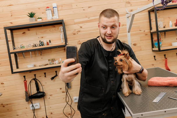 Peluquero masculino profesional haciendo foto con el cliente del perro después del procedimiento de aseo en el salón de animales - Foto, Imagen