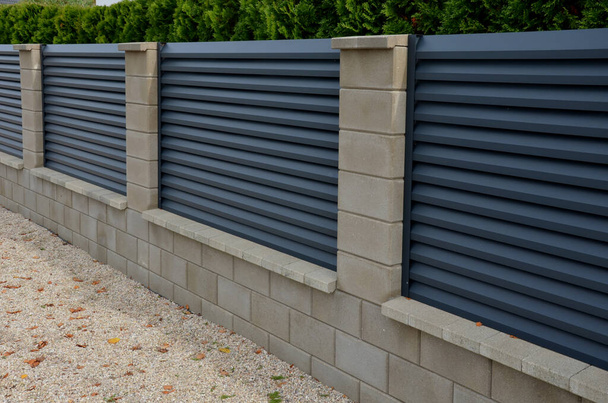 fém tömések a kerítés egy alátét beton blokkok. A fém alumínium kerítés biztosítja a magánélet a kertben. A vízszintes lécek jól fedik. a tujiból készült sövény védelmet nyújt - Fotó, kép