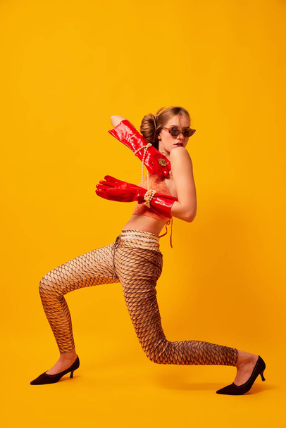 Weird people concept. Creative portrait of young girl in avant-garde style image isolated over bright yellow background. Vivid style, queer, art, fashion Stylish model in bright red gloves. - Photo, Image
