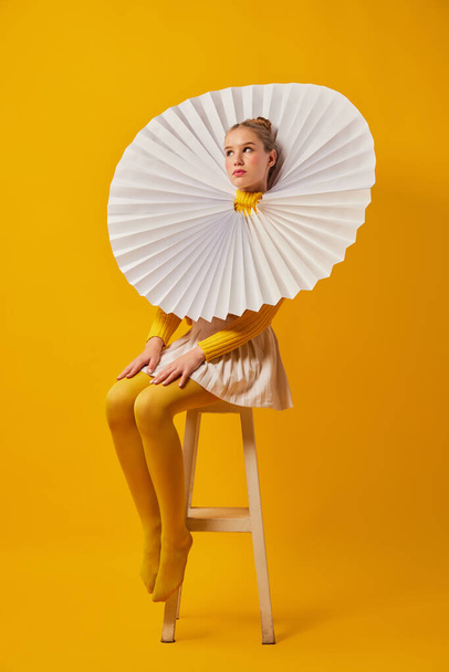 Young indifferent girl in giant jabot collar or neckwear and yellow tights isolated over yellow background. Contemporary art, weird beauty, avant-garde fashion. - Zdjęcie, obraz