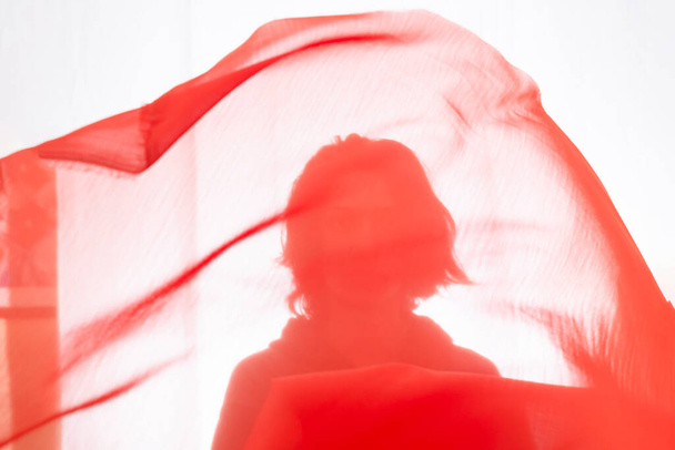 Young man with red transparent fabric in motion against white background. Studio photography. - Фото, зображення