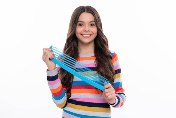 Teenager brushing combing hair with big comb on yellow isolated studio background. Teen girl with hairbrush. Kids hairstyle. Happy girl face, positive and smiling emotions - Photo, Image