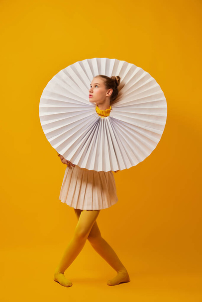 Music. Young indifferent girl in giant jabot collar or neckwear and yellow tights isolated over yellow background. Contemporary art, weird beauty, avant-garde fashion. - Φωτογραφία, εικόνα